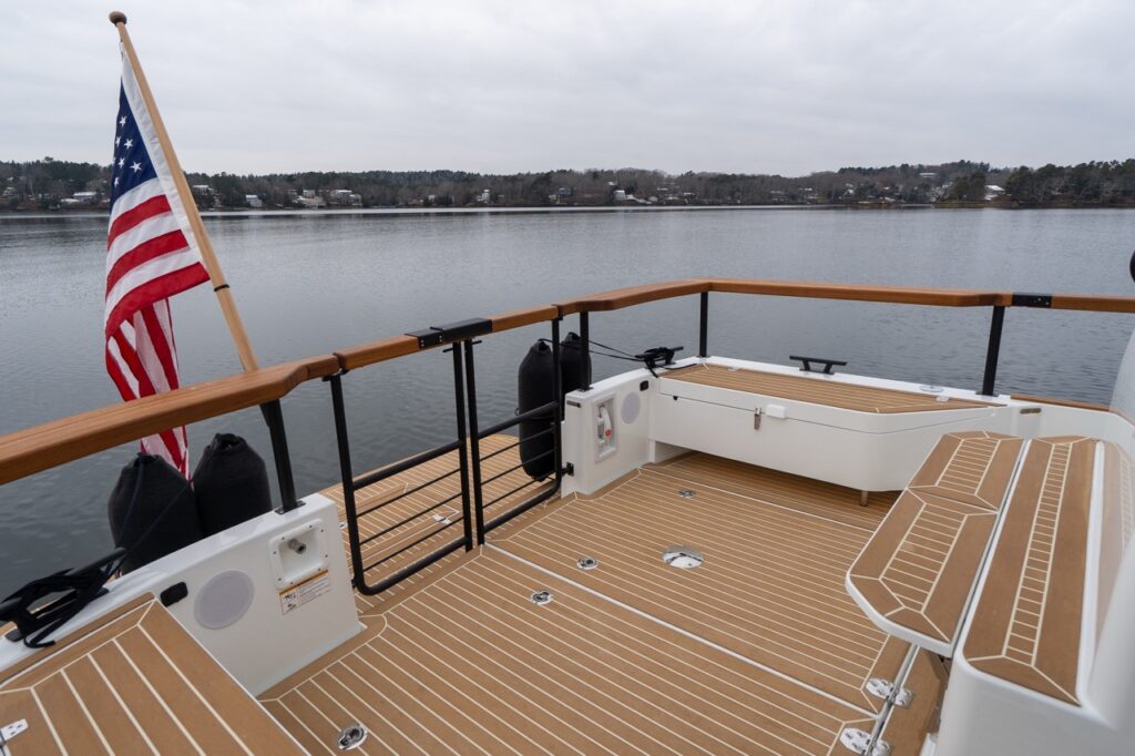 Aft cockpit of the Targa 32 with synthetic teak decking, fold-down transom seating, teak-capped railings, integrated fender storage, and an American flag at the stern overlooking calm water.