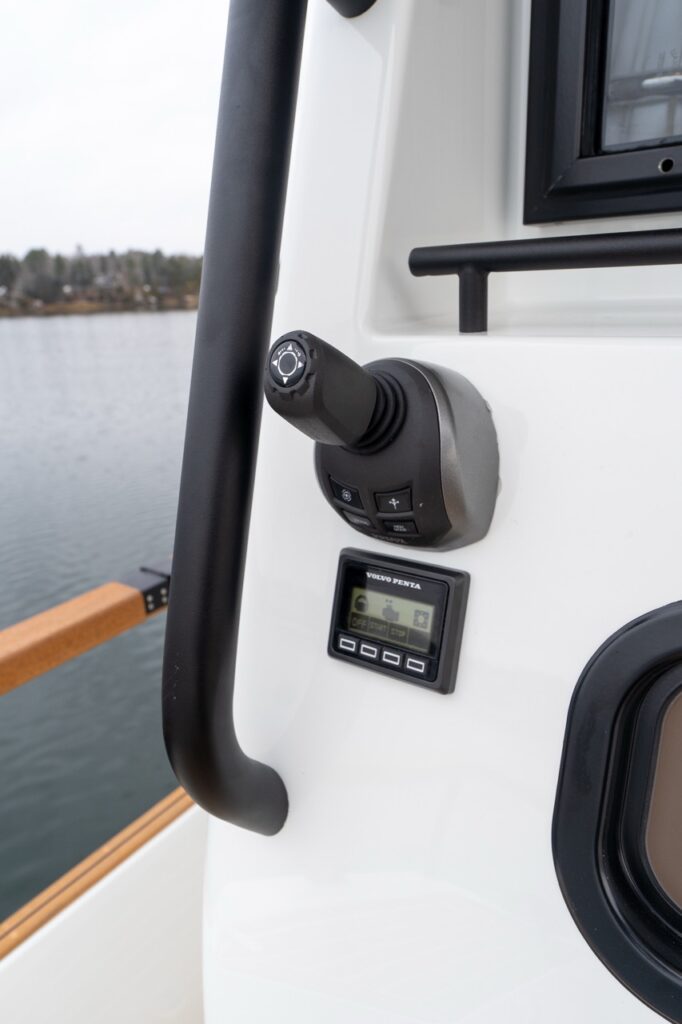 Close-up of the Targa 32’s exterior joystick docking control and Volvo Penta engine control display mounted at the aft cockpit side station, with teak handrail and water visible in the background.