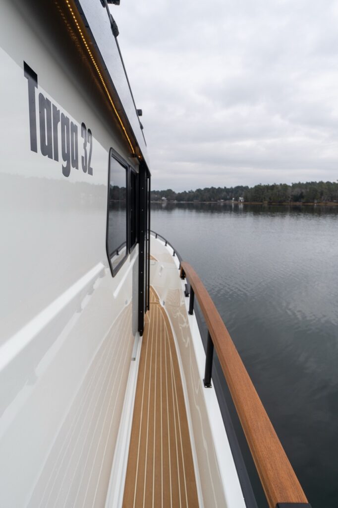 Walkaround side deck on a Targa 32 showing teak handrail, non-skid decking, and cabin side with Targa 32 branding, overlooking calm water.