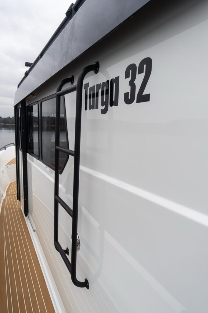Close-up of the starboard side of a Targa 32 showing the black exterior side ladder mounted beside the pilothouse windows, with “Targa 32” model badging on the white hull side above the teak-patterned walkaround deck.