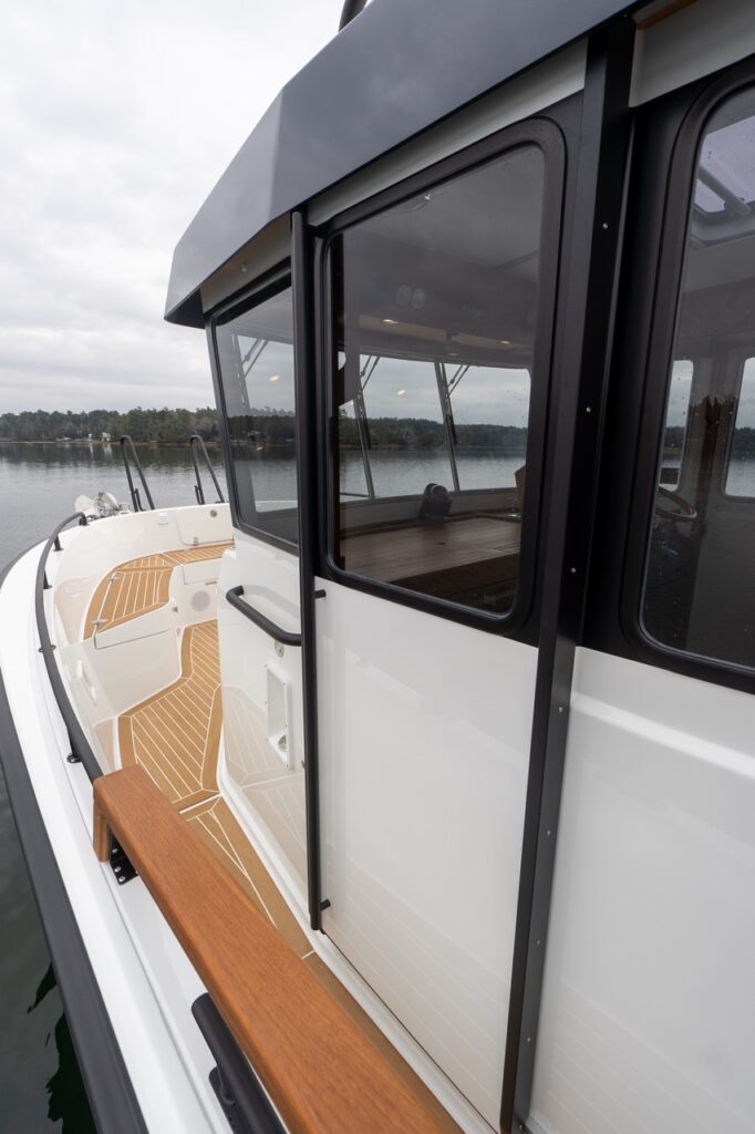 Starboard-side walkaround deck on a Targa 32 showing the cabin side windows, teak-topped side bench, secure handholds, and teak-patterned non-skid decking leading forward toward the bow.