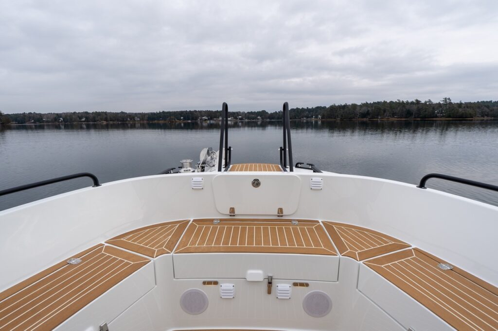Forward-facing view from the Targa 32 bow seating area, showing wraparound molded benches with teak-style decking, integrated speakers, and black safety rails overlooking calm water.