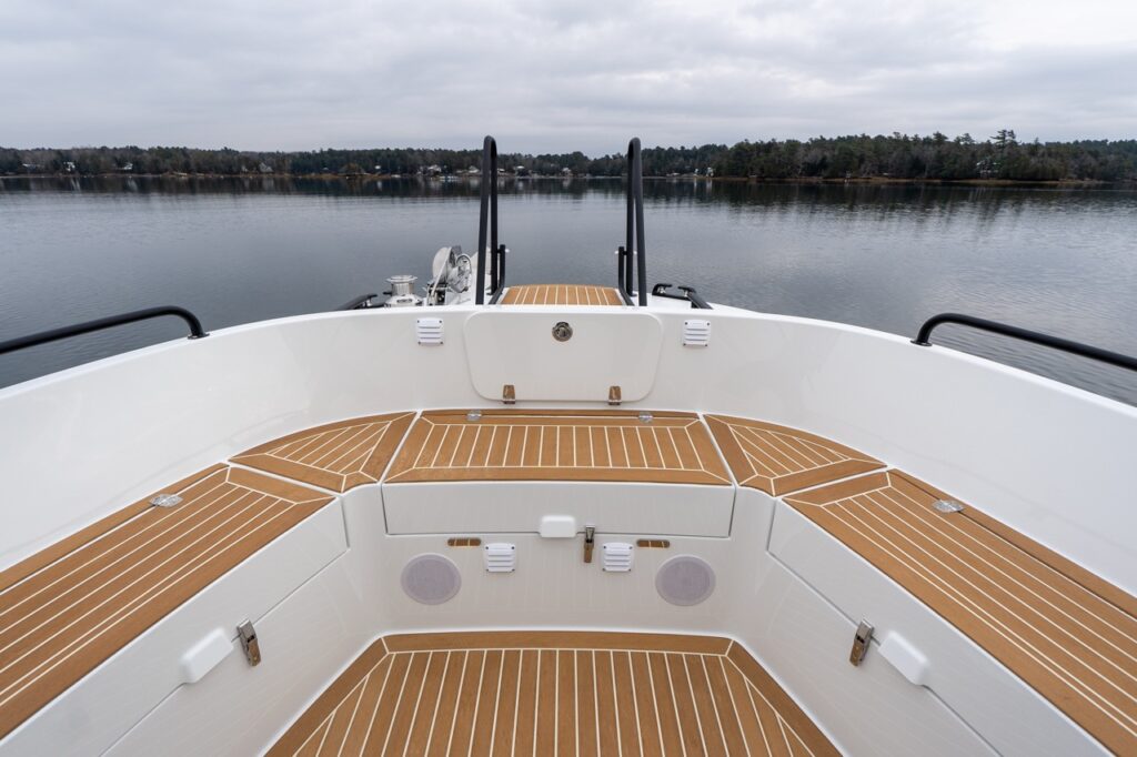 Forward bow seating area of the Targa 32 featuring wraparound molded seating with teak-patterned decking and cushions, looking forward toward the bow rails over calm water.