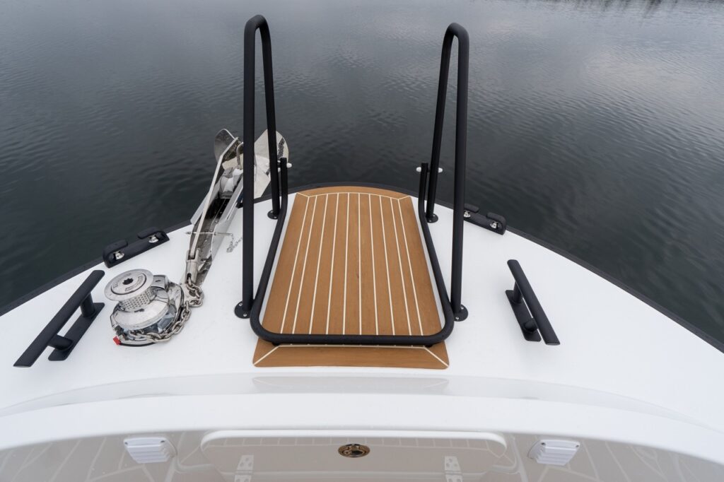 Forward foredeck of the Targa 32 showing the teak-patterned bow platform with integrated safety rails, anchor windlass, anchor, and mooring cleats, viewed looking straight ahead over calm water.