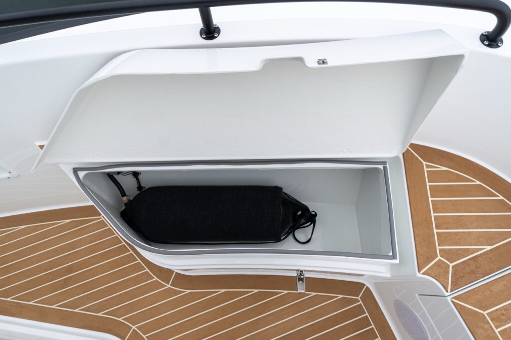 Foredeck fender locker on the Targa with the hatch open, showing a deep molded storage compartment holding a black cylindrical fender, surrounded by synthetic teak decking.