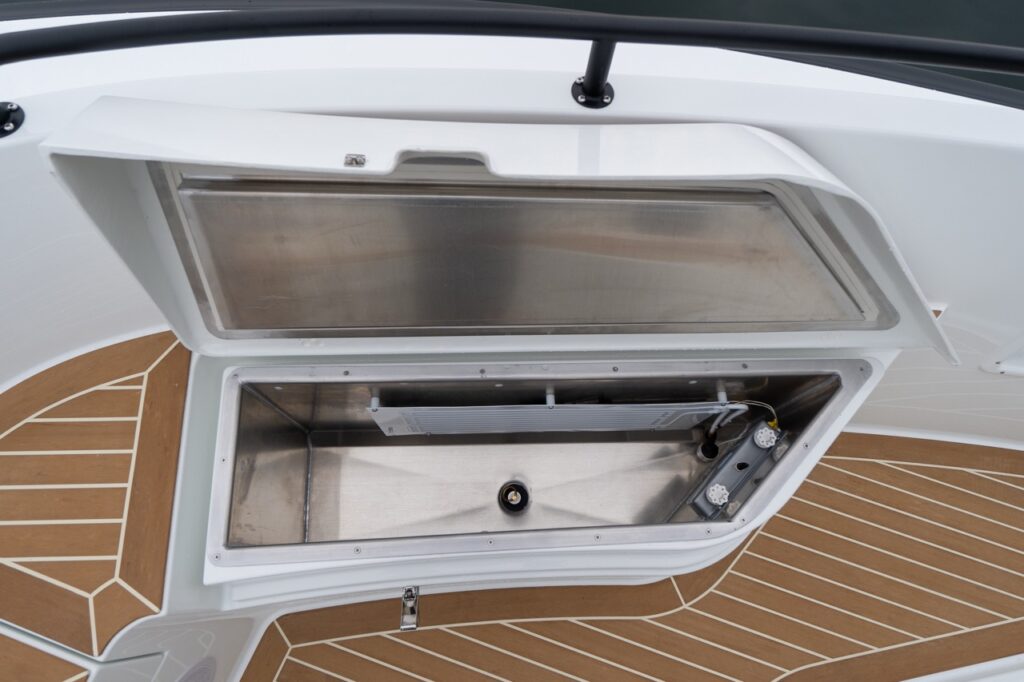 Open fender locker on the foredeck of the Targa, showing a stainless-lined storage compartment set into the deck with a hinged hatch above and synthetic teak decking surrounding it.