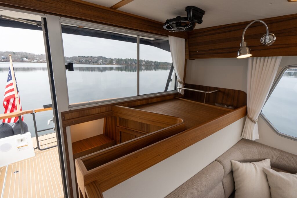 Interior view of the Targa 32 pilothouse showing the aft-facing galley module with teak countertops and storage, positioned beside the sliding aft door and large windows overlooking the water.