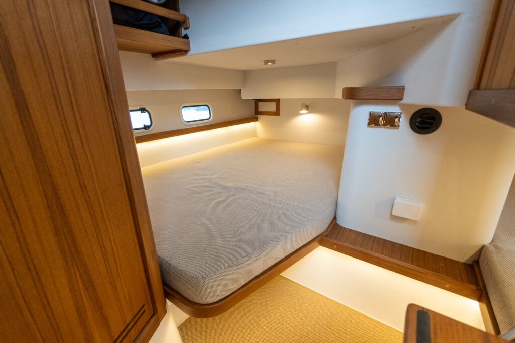 Aft cabin double berth on the Targa 32, featuring a wide upholstered mattress, teak trim, hull-side portlights, integrated reading light, and warm LED accent lighting beneath the berth platform.