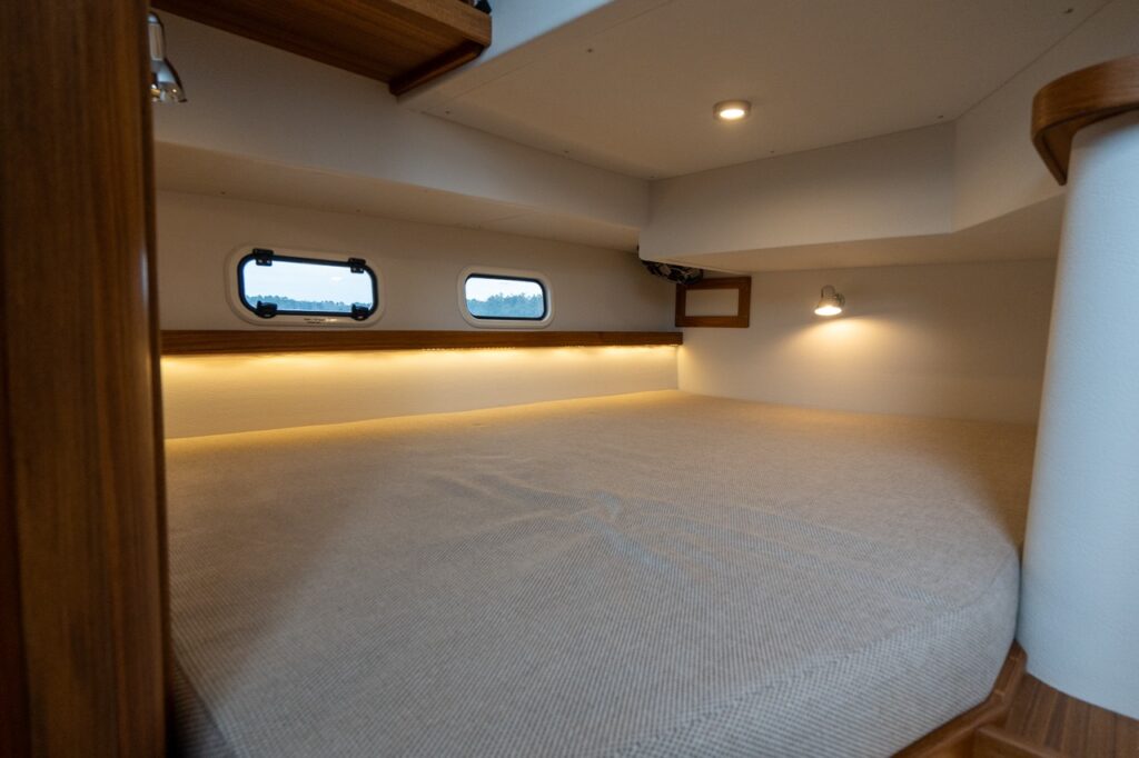 Aft double berth on the Targa 32 featuring a full-width mattress, warm teak trim, hull-side windows, and soft indirect LED lighting.