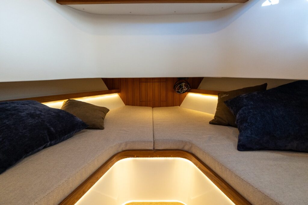 V-berth sleeping area in the standard forward cabin of the Targa 32, showing twin berth cushions with accent pillows and warm indirect LED lighting.