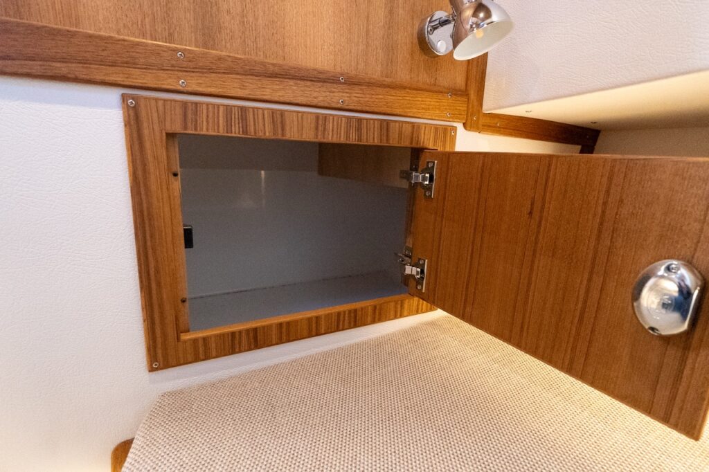 Open storage locker in the forward V-berth cabin of the Targa 32, showing teak cabinetry with a hinged door and integrated berth-side storage.
