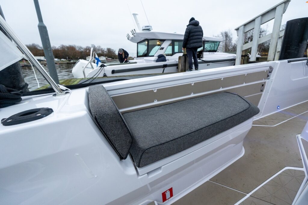 Forward-facing fender box bench seat on the port side of the Axopar 38 aft deck with padded backrest, positioned near the side gate for easy dock access.