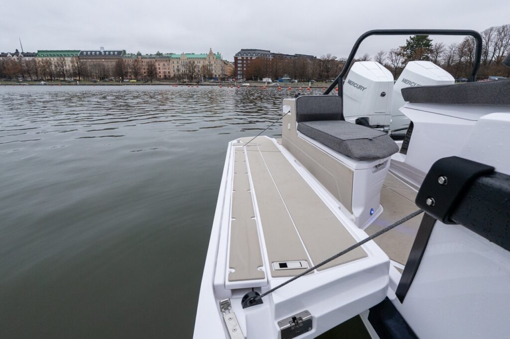 Starboard-side activity platform on the Axopar 38 shown deployed alongside the aft deck, featuring a wide non-skid step, support cable, and adjacent forward-facing fender box bench seat near the twin Mercury outboards.