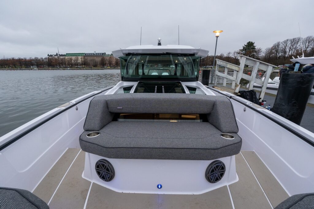 Forward deck seating area on the Axopar 38 showing the forward-facing bench seat positioned in front of the forward cabin, with integrated cupholders, speakers, and wide walkaround decks on both sides.
