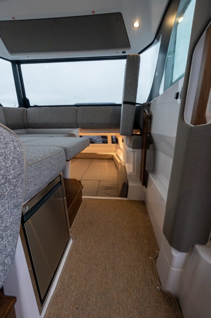 View inside the Axopar 38 pilothouse showing access to the aft cabin through the aft bench seat, with surrounding lounge seating, wide walkways, and large windows creating an open, functional interior.