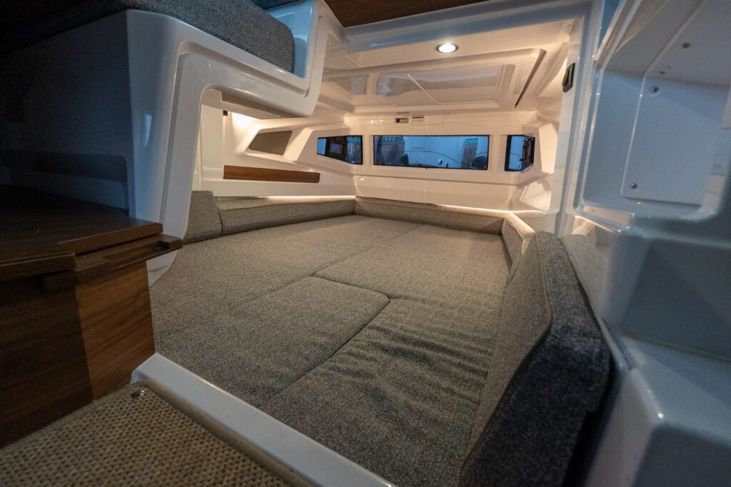 Interior view of the Axopar 38 aft cabin showing a spacious double berth with upholstered cushions, integrated ambient lighting, side windows, and clean Nordic interior finishes.