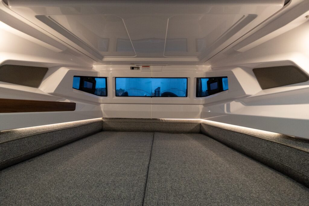 Aft cabin berth in the Axopar 38 showing a wide, flat sleeping area with upholstered side bolsters, integrated ambient lighting, and side windows providing natural light and ventilation.