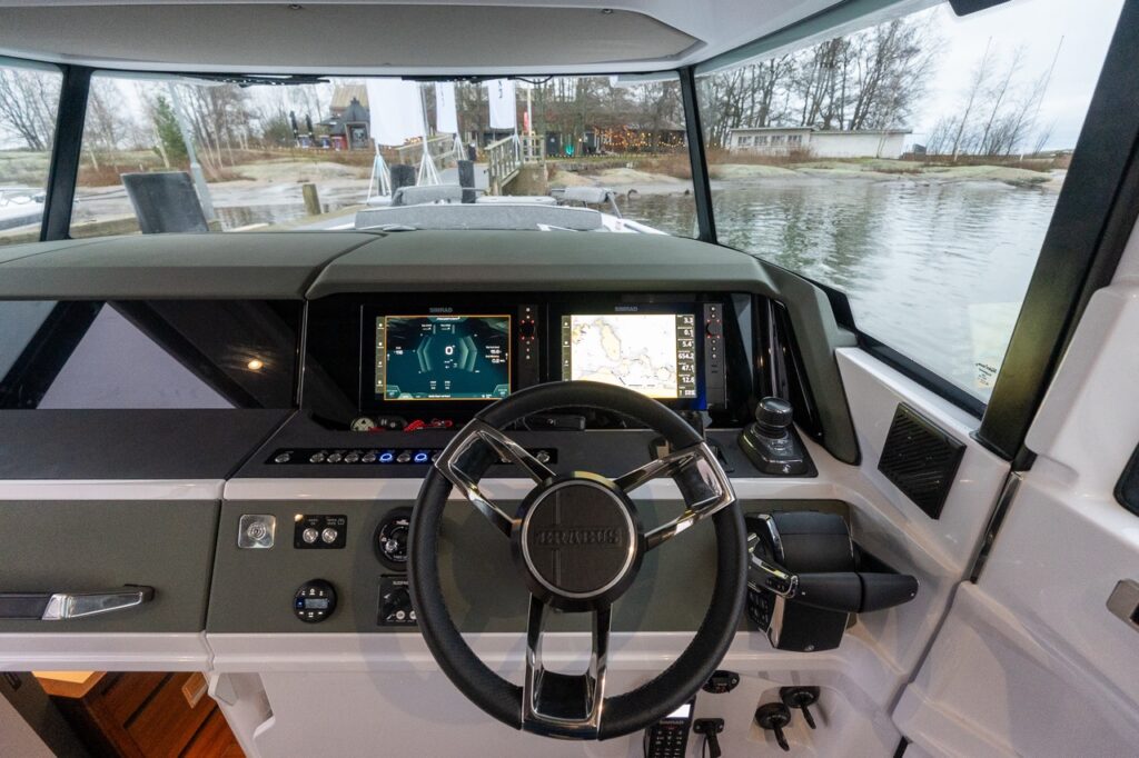 Wide view of the Axopar 38 BRABUS Edition helm showing the BRABUS steering wheel, dual Simrad Multi Function Displays (MFDs), Mercury throttle and joystick controls, and panoramic pilothouse windshield with clear sightlines ahead.