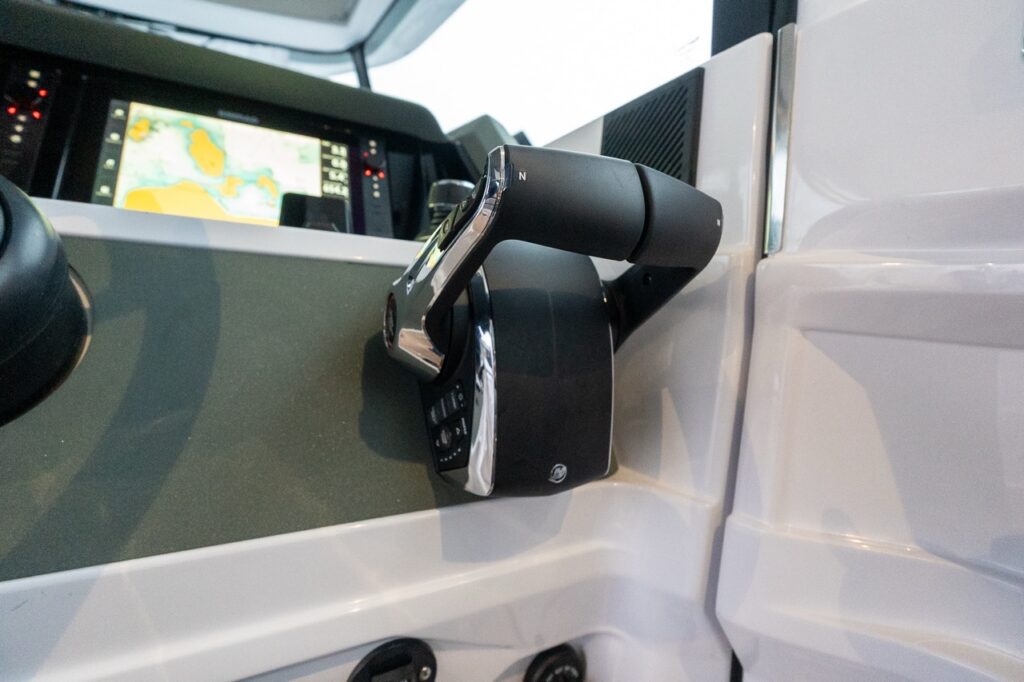 Close-up of the Axopar 38 helm throttle control showing the Mercury electronic throttle and shift lever mounted beside the helm, with the navigation display visible in the background.