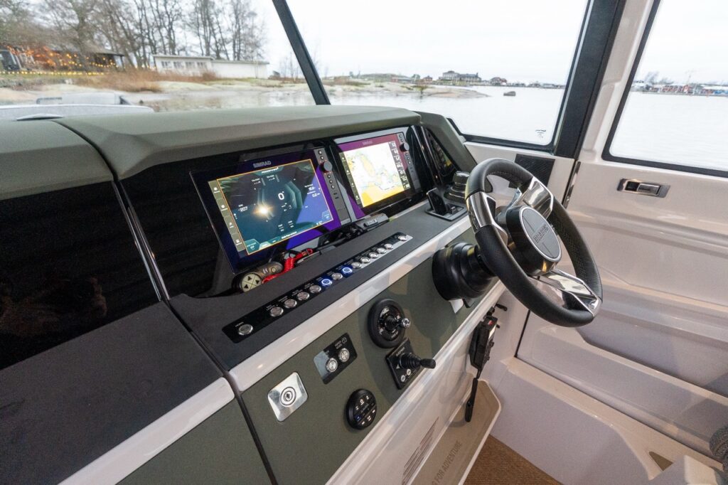 Helm station of the all-new Axopar 38 featuring dual Multi Function Displays (MFDs), a modern steering wheel, intuitive controls, and excellent visibility through the pilothouse windshield with water views ahead.