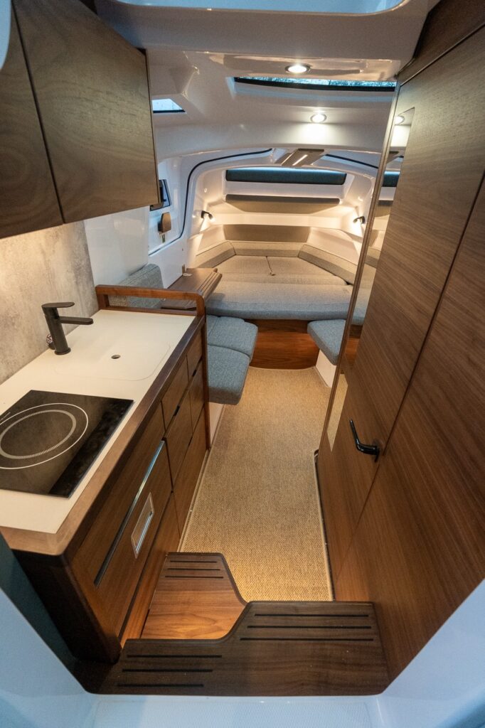 Forward cabin of the all-new Axopar 38 featuring a compact galley, separate enclosed head compartment, and a forward seating area that converts into a comfortable berth, finished in warm wood tones and modern upholstery.
