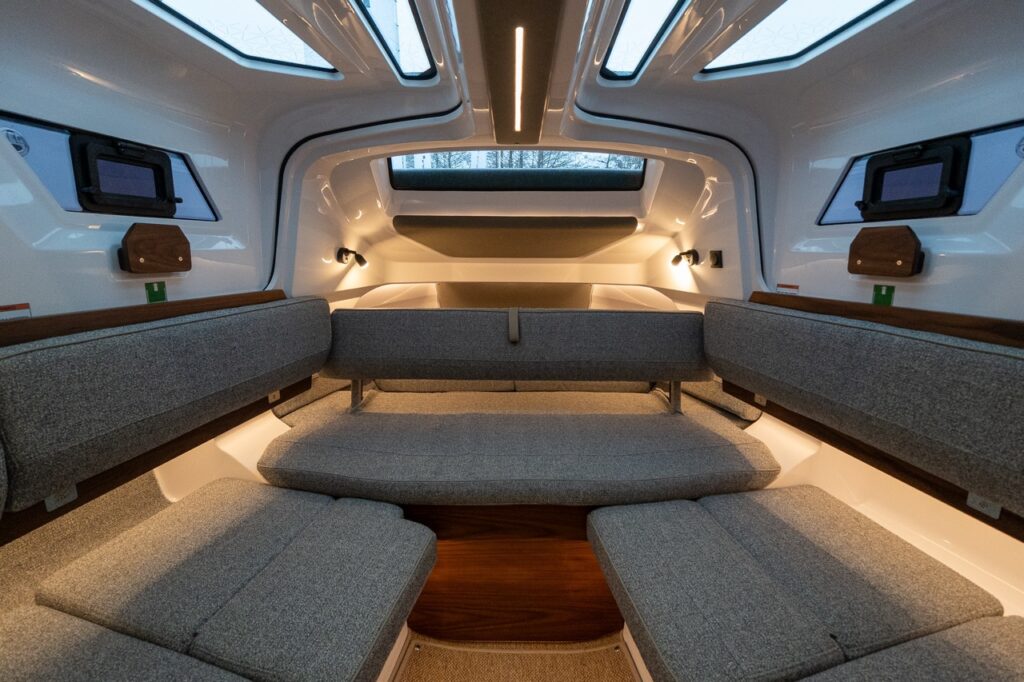 Axopar 38 forward cabin seating configuration with opposing benches, overhead skylights, warm LED lighting, and Nordic interior finishes creating a bright, social cabin space.