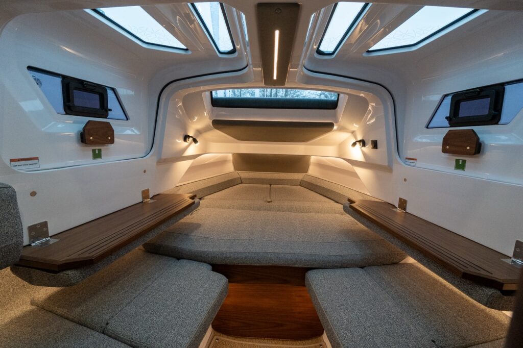 Axopar 38 forward cabin sleeping area with twin berths, overhead skylights, warm LED lighting, and opening side windows creating a bright, spacious interior.
