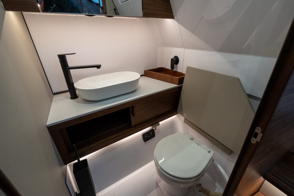 Axopar 38 separate head compartment showing enclosed marine toilet, vessel sink with matte black faucet, Nordic wood cabinetry, and integrated storage in the forward cabin.