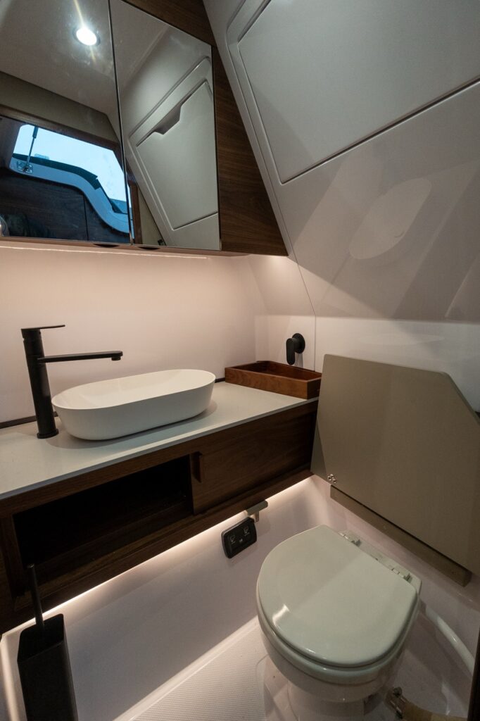 Separate head compartment in the Axopar 38 forward cabin featuring a vessel sink, matte black faucet, enclosed marine toilet, mirror, and Nordic wood cabinetry.