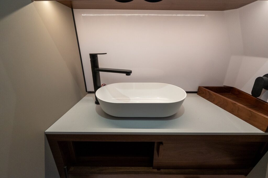 Vessel-style sink with matte black faucet in the separate head compartment of the Axopar 38 forward cabin, featuring Nordic interior design and built-in storage.