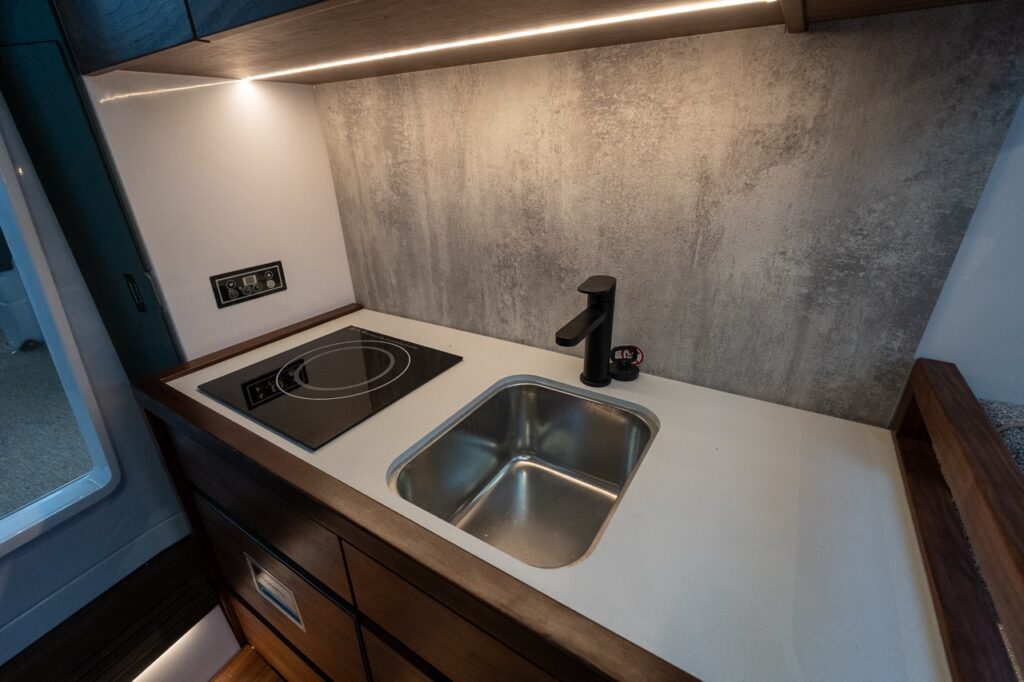 Axopar 38 forward cabin galley with induction cooktop, stainless steel sink, modern cabinetry, and integrated LED lighting below deck.