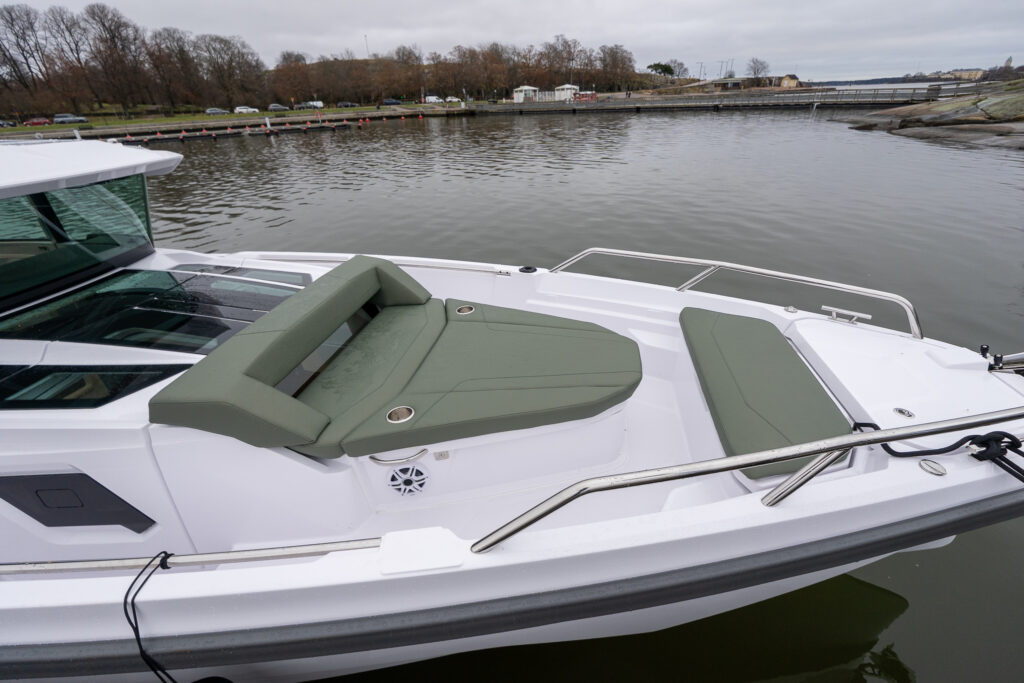 Axopar 38 forward deck sunbed with hunter green cushions and forward bench seat, viewed from above along the starboard side.