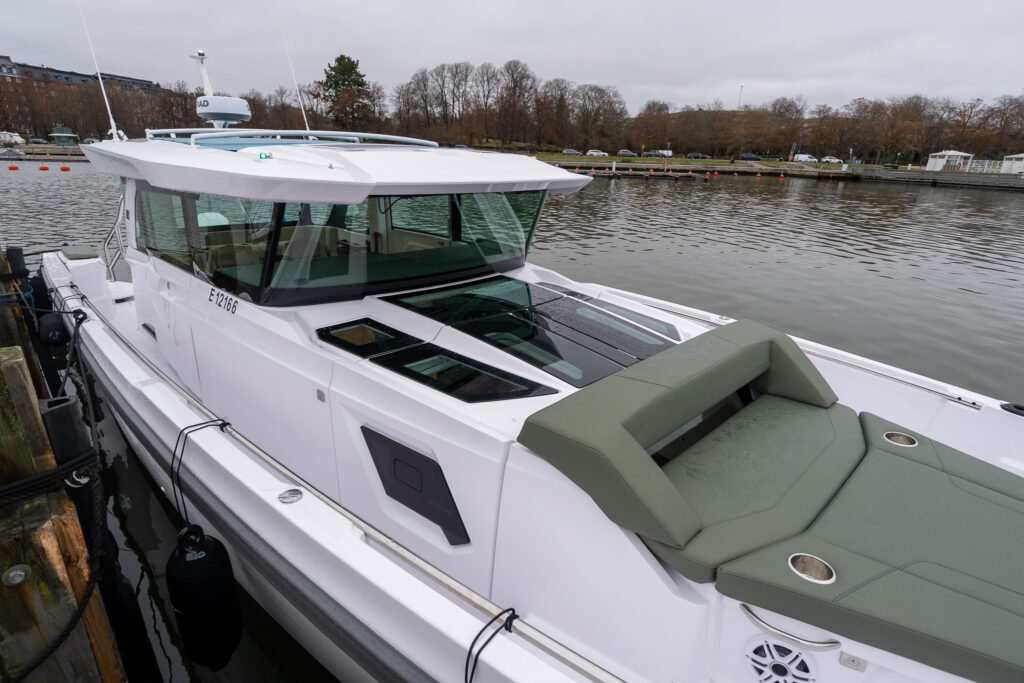 Forward cabin roof and sunbed on an Axopar 38 with hunter green cushions, viewed from the starboard side alongside the dock.