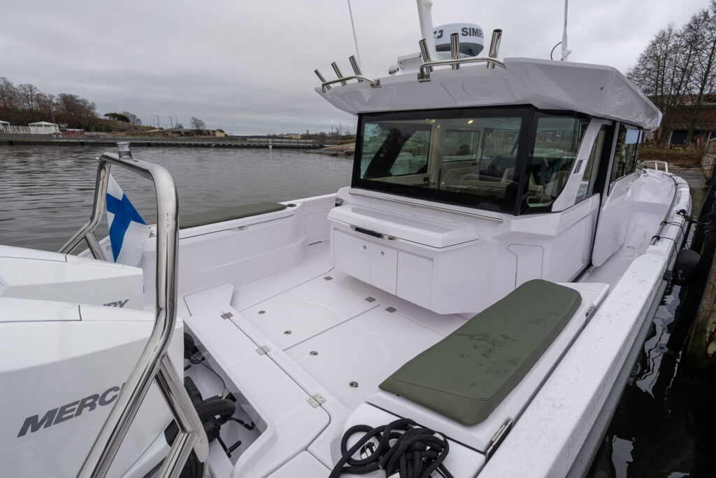 Aft cockpit wet bar with hunter green fenderbox bench cushions and twin white outboard engines on an Axopar 38, viewed from the stern looking forward toward the pilothouse.