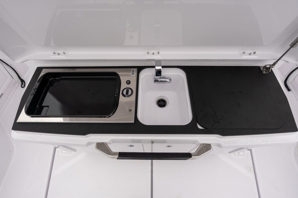 Axopar 38 aft wet bar fully open showing integrated sink, faucet, removable prep surface, and concealed cooktop beneath.