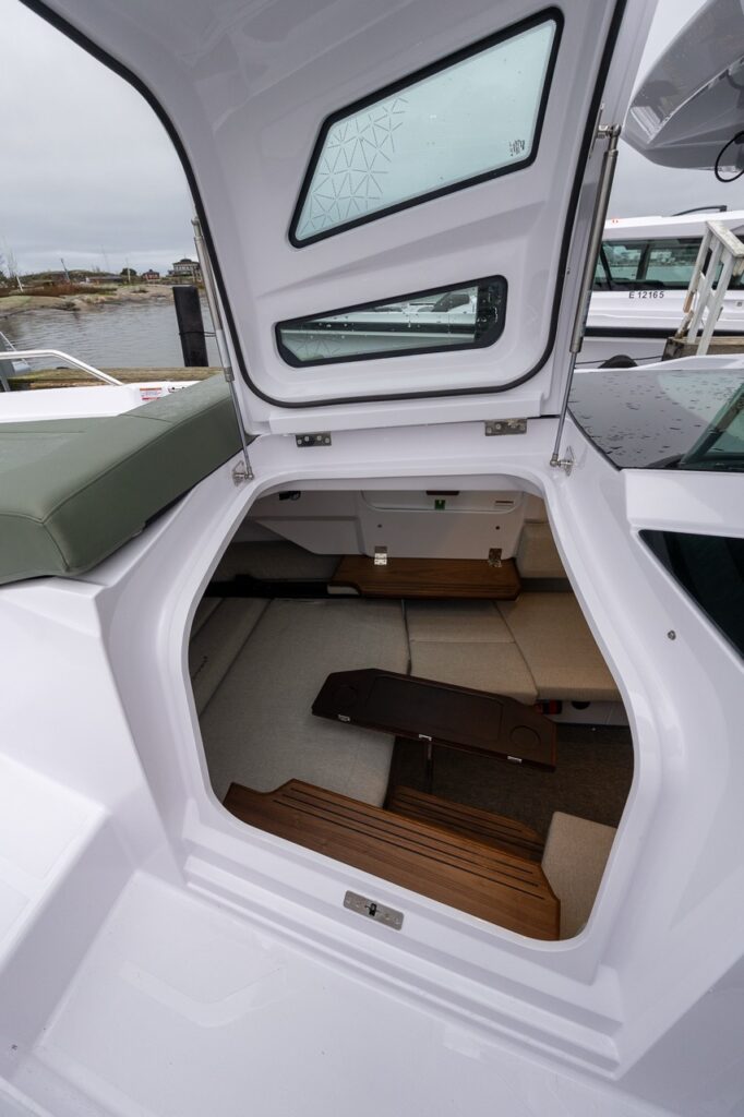Axopar 38 gullwing door open, looking down into the forward cabin with convertible seating, wood steps, and natural light from overhead windows.
