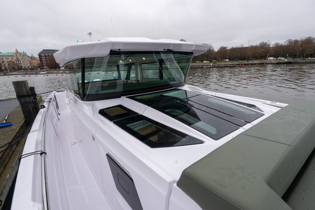 Axopar 38 viewed looking aft over the forward cabin roof, showing the opening aft window, large roof glazing, hunter green exterior upholstery, and pilot house during Axopar 38 media day in Finland.
