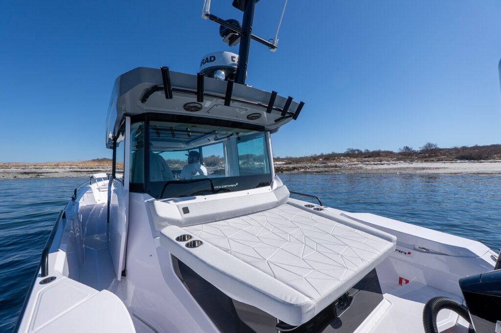 Axopar 29 aft deck sunbed in Chalk upholstery behind the pilothouse with rod holders and radar mast