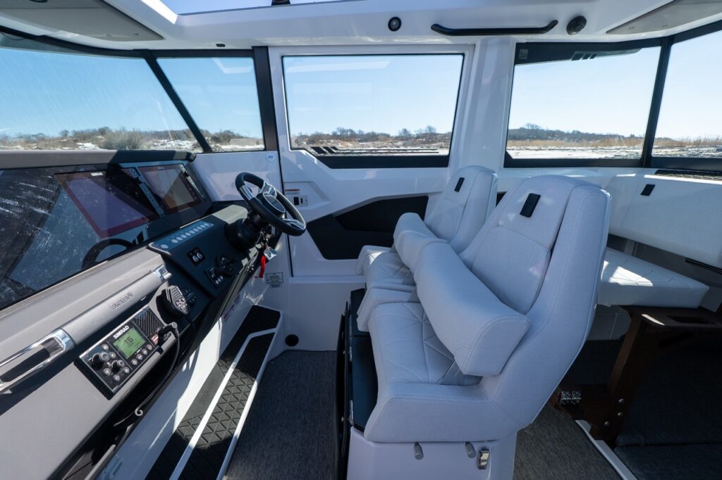 Axopar 29 XC Cross Cabin pilothouse interior showing helm dashboard, twin helm seats, and cabin seating