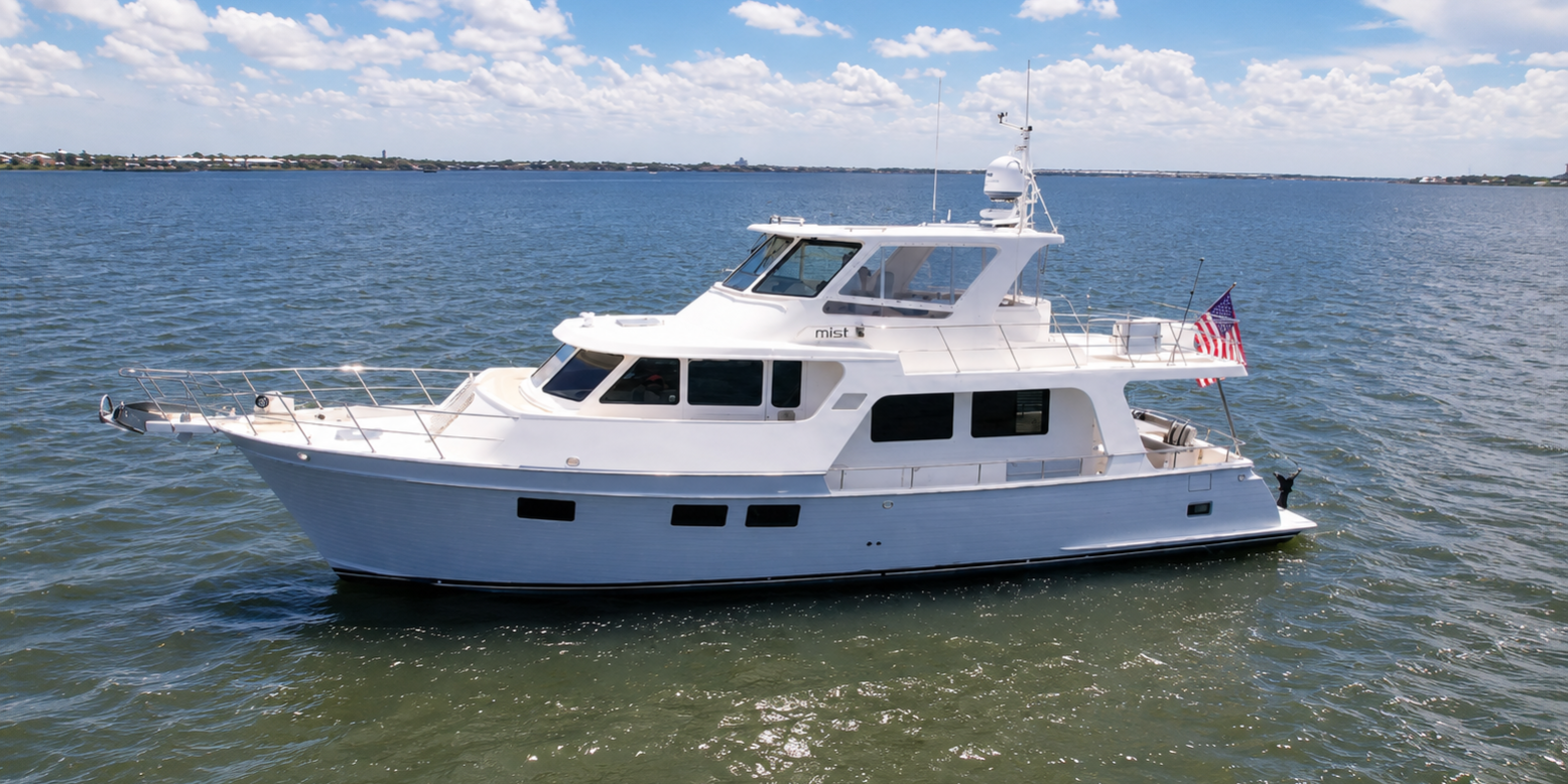 Aerial port-side view of the 2018 Marlow 53E Mist cruising on calm coastal waters, showcasing her gray hull, semi-enclosed flybridge, and owner-operator cruising design.