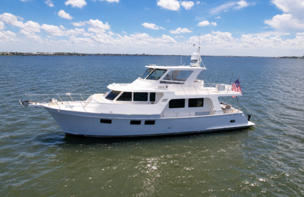 Aerial port-side view of the 2018 Marlow 53E Mist cruising on calm coastal waters, showcasing her gray hull, semi-enclosed flybridge, and owner-operator cruising design.