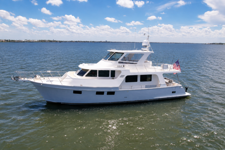 Aerial port-side view of the 2018 Marlow 53E Mist cruising on calm coastal waters, showcasing her gray hull, semi-enclosed flybridge, and owner-operator cruising design.